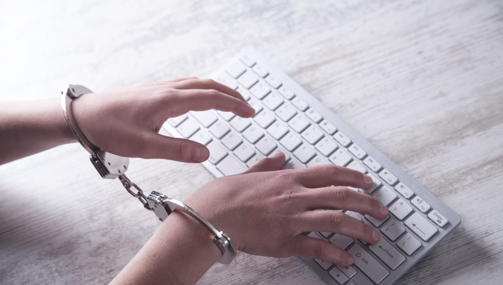 Hands in handcuffs typing on keyboard. Cyber Crime
